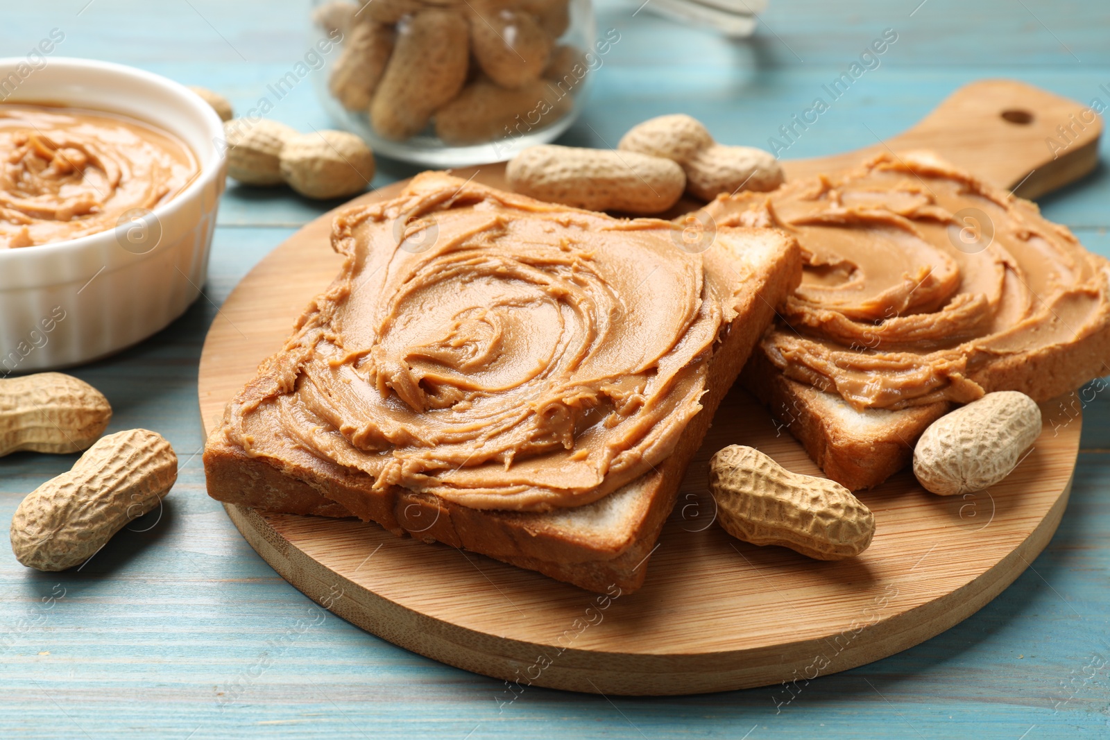 Photo of Tasty sandwiches with peanut butter and nuts on light blue wooden table, closeup