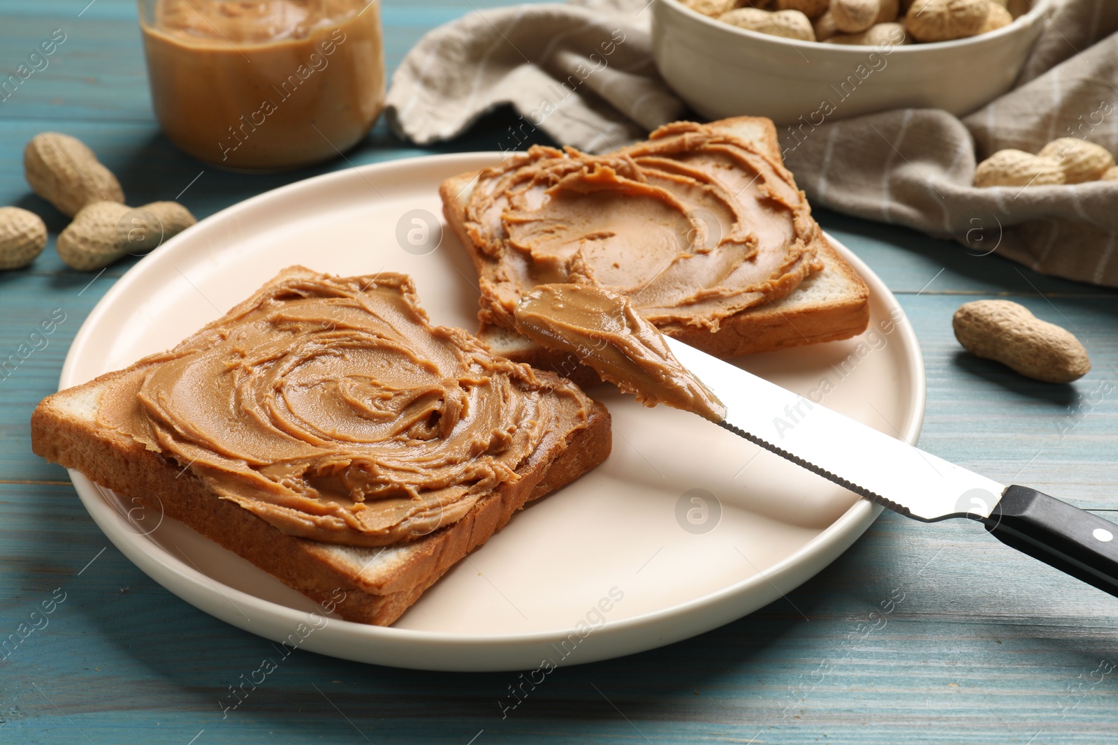 Photo of Tasty sandwiches with peanut butter and nuts on light blue wooden table, closeup