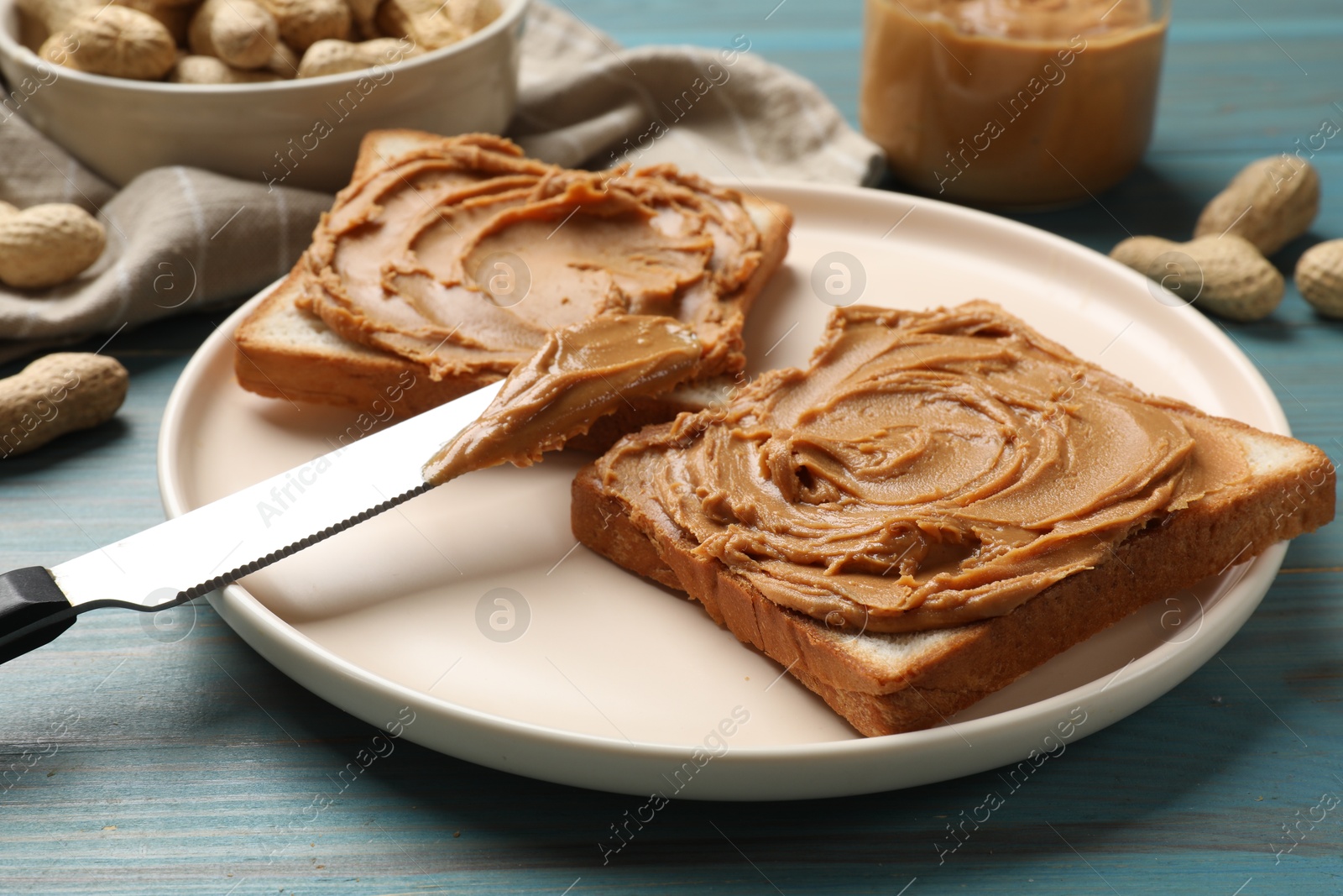 Photo of Tasty sandwiches with peanut butter and nuts on light blue wooden table, closeup