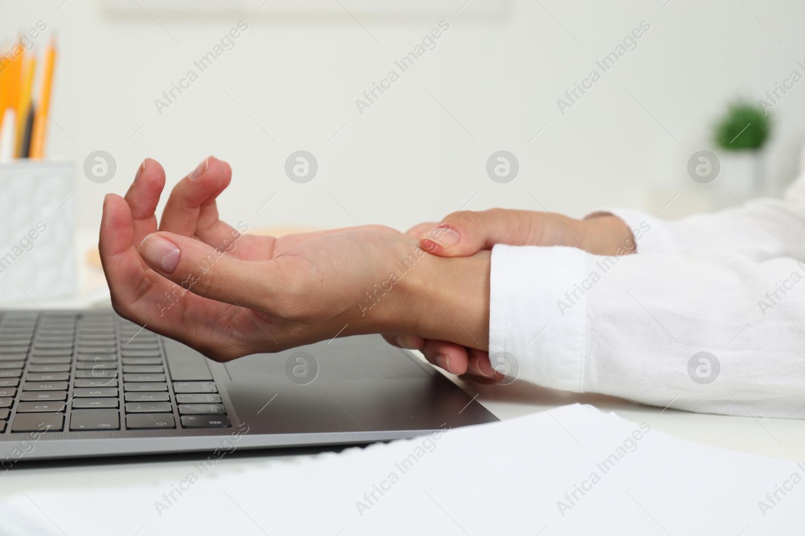 Photo of Carpal tunnel syndrome. Woman suffering from pain in wrist at desk indoors, closeup