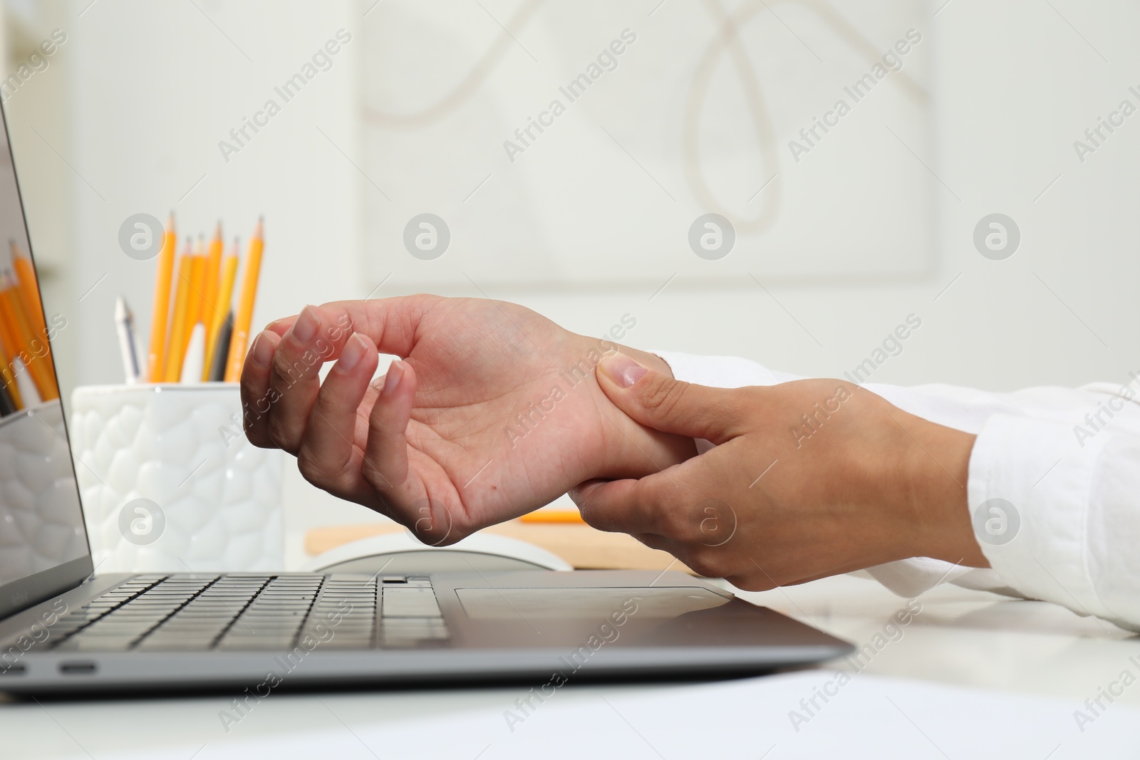 Photo of Carpal tunnel syndrome. Woman suffering from pain in wrist at desk indoors, closeup