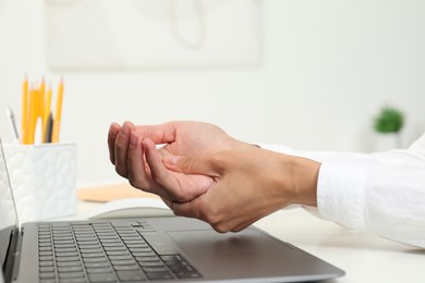 Photo of Carpal tunnel syndrome. Woman suffering from pain in wrist at desk indoors, closeup