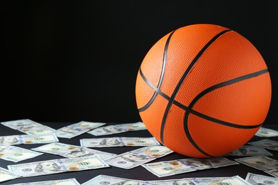 Photo of Basketball ball and dollar banknotes on black table