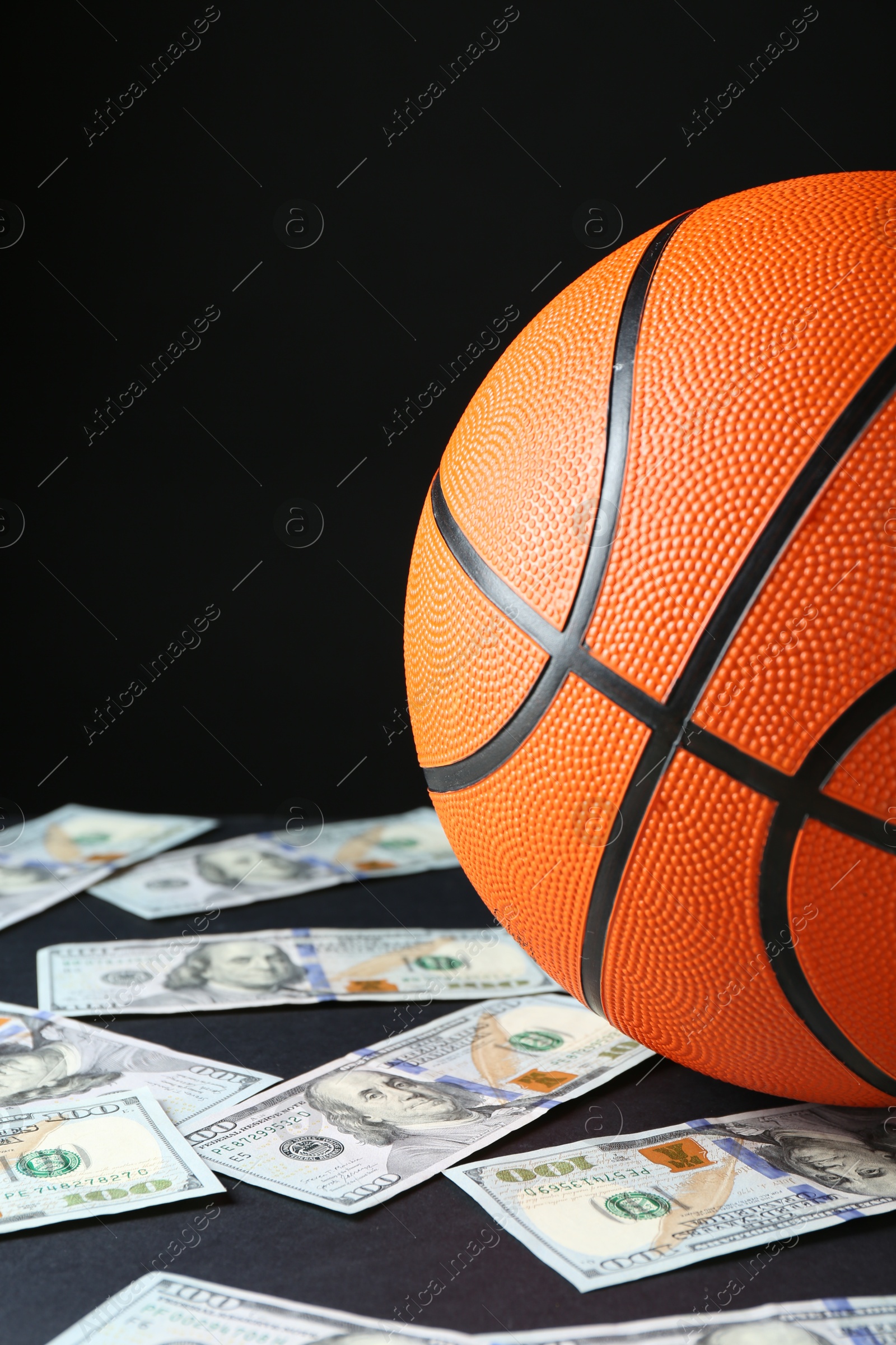 Photo of Basketball ball and dollar banknotes on black table, closeup