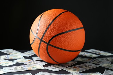 Photo of Basketball ball and dollar banknotes on black table