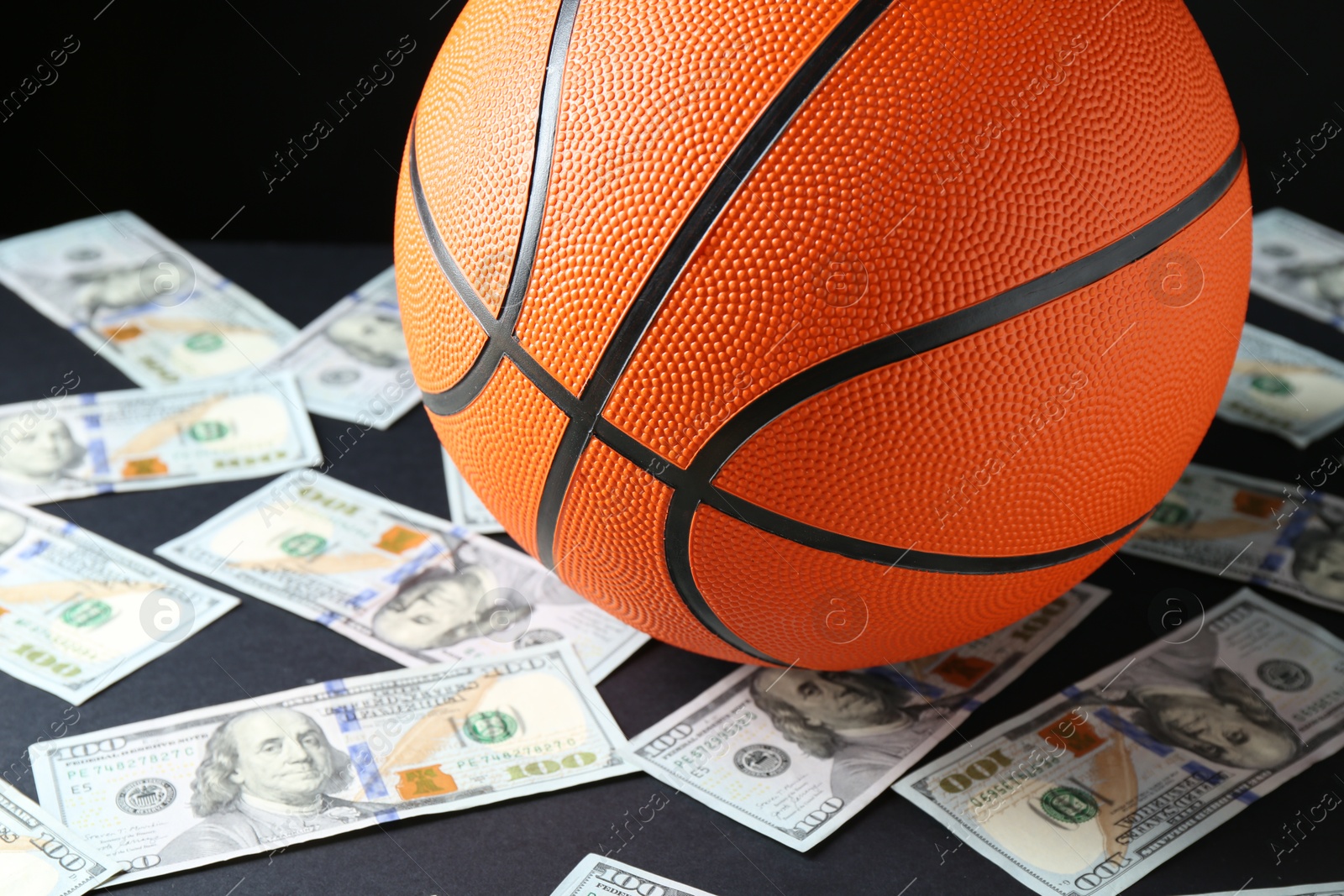 Photo of Basketball ball and dollar banknotes on black table, closeup