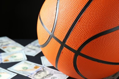 Photo of Basketball ball and dollar banknotes on black table, closeup