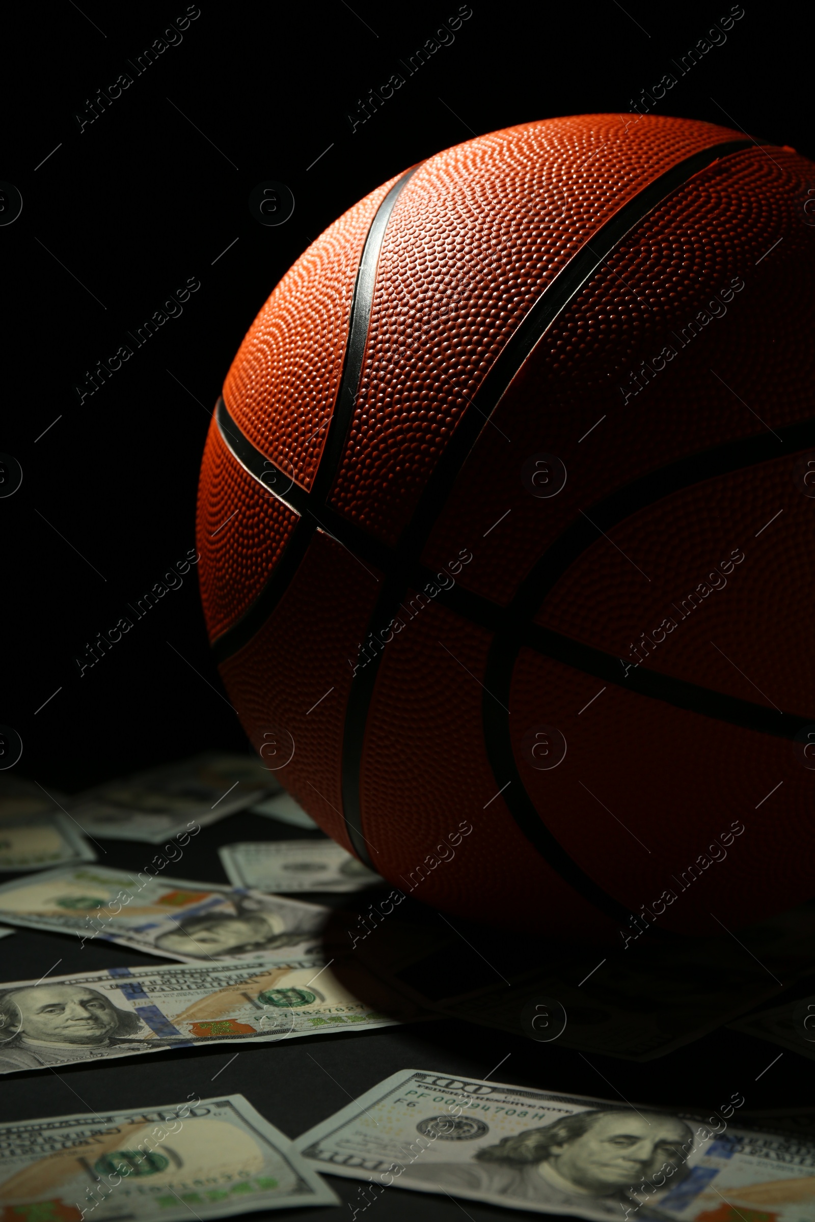 Photo of Basketball ball and dollar banknotes on black table, closeup