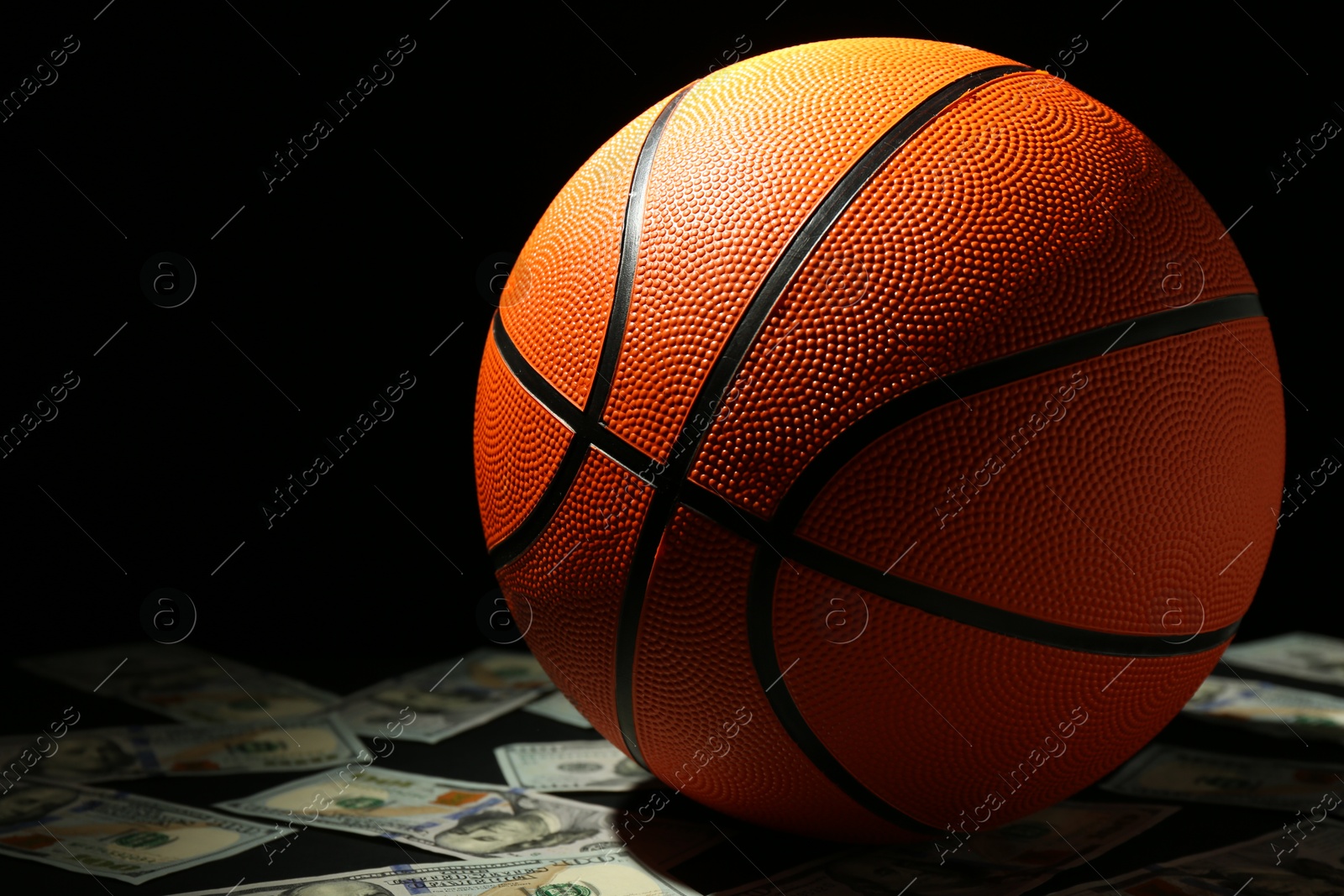 Photo of Basketball ball and dollar banknotes on black table, closeup