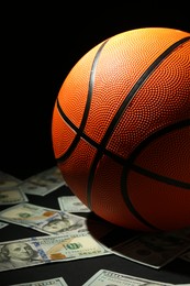 Photo of Basketball ball and dollar banknotes on black table, closeup