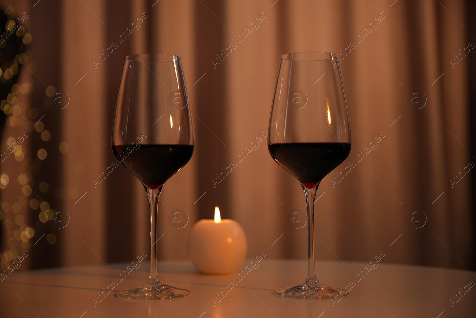 Photo of Burning candle and wine in glasses on table indoors