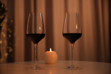 Photo of Burning candle and wine in glasses on table indoors