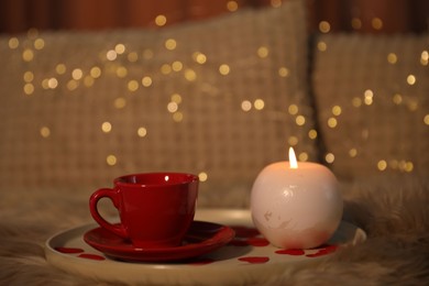 Burning candle, cup of drink and rose petals on bed indoors