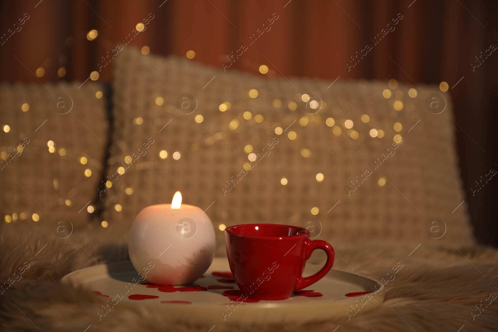 Photo of Burning candle, cup of drink and rose petals on bed indoors