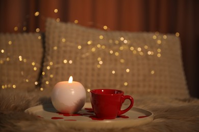 Burning candle, cup of drink and rose petals on bed indoors