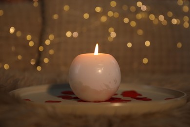 Burning candle and rose petals on bed indoors