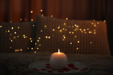 Burning candle and rose petals on bed indoors