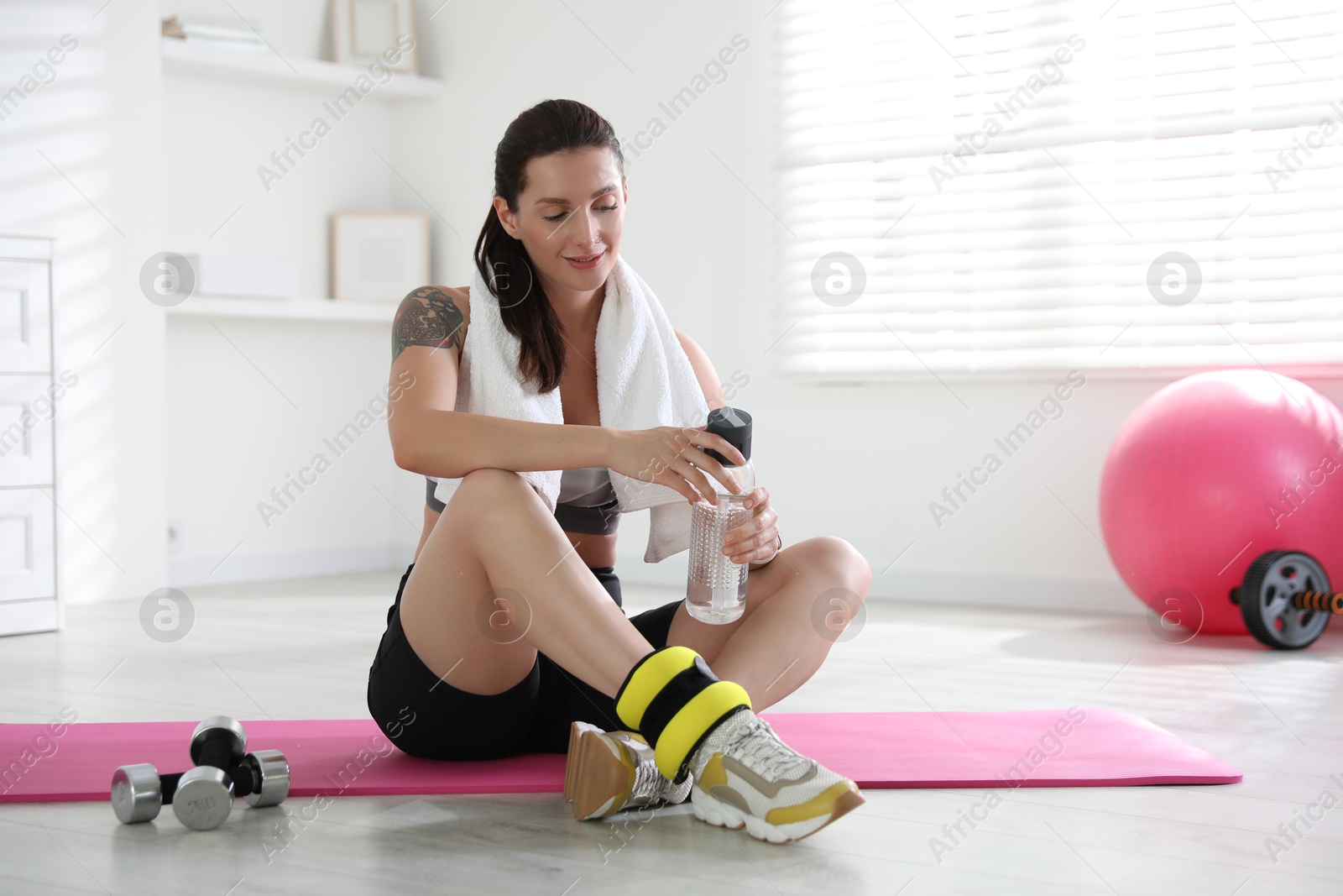 Photo of Beautiful woman with ankle weights and bottle of water indoors