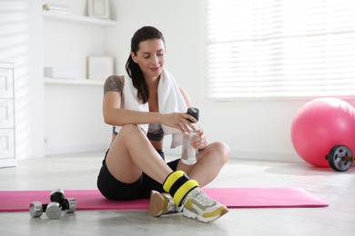 Beautiful woman with ankle weights and bottle of water indoors