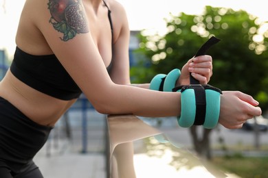 Photo of Woman putting ankle weight on her arm outdoors, closeup