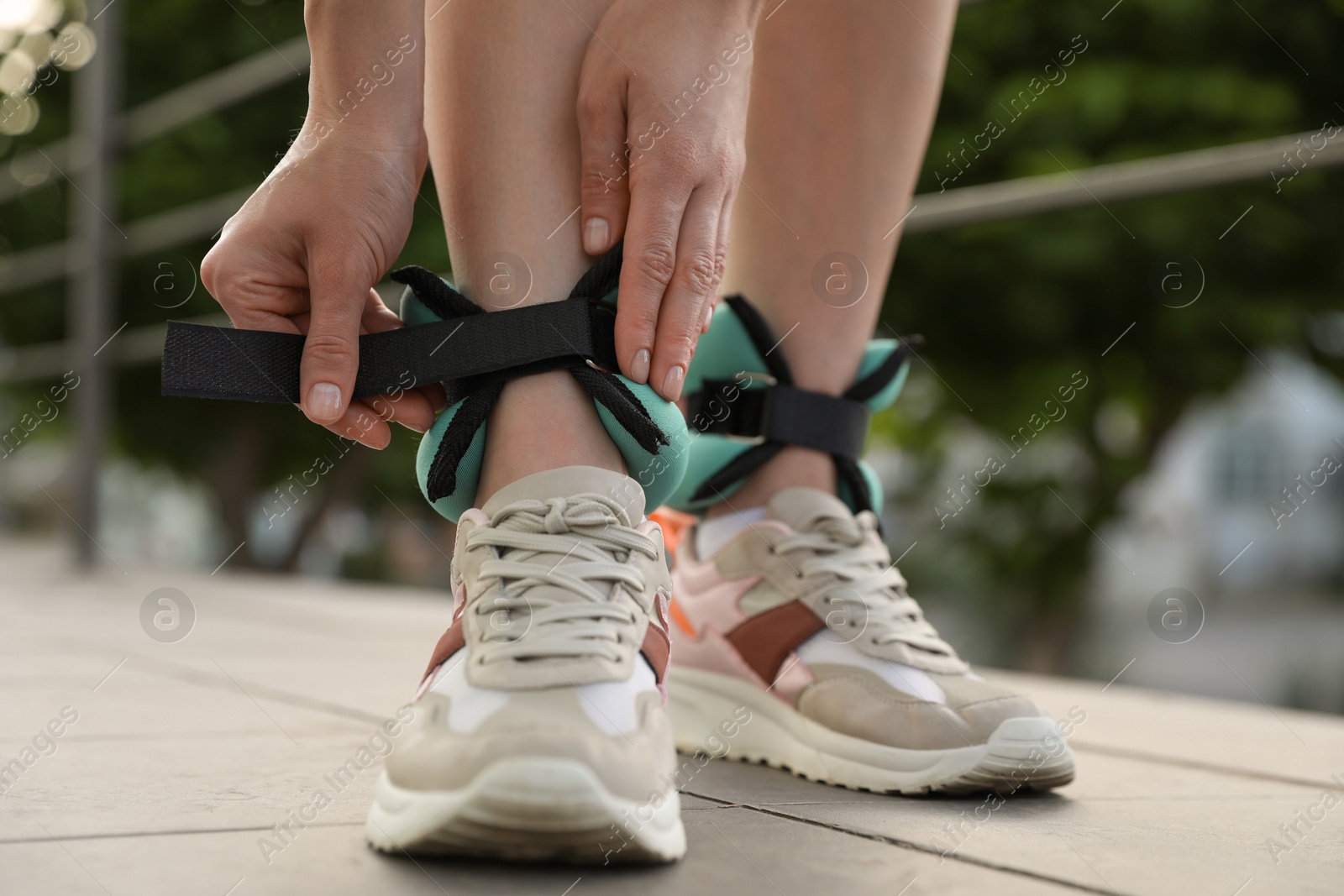 Photo of Woman putting on ankle weights outdoors, closeup