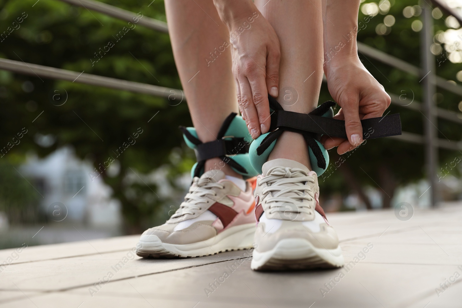 Photo of Woman putting on ankle weights outdoors, closeup