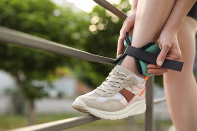 Woman putting on ankle weight outdoors, closeup