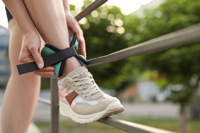 Photo of Woman putting on ankle weight outdoors, closeup