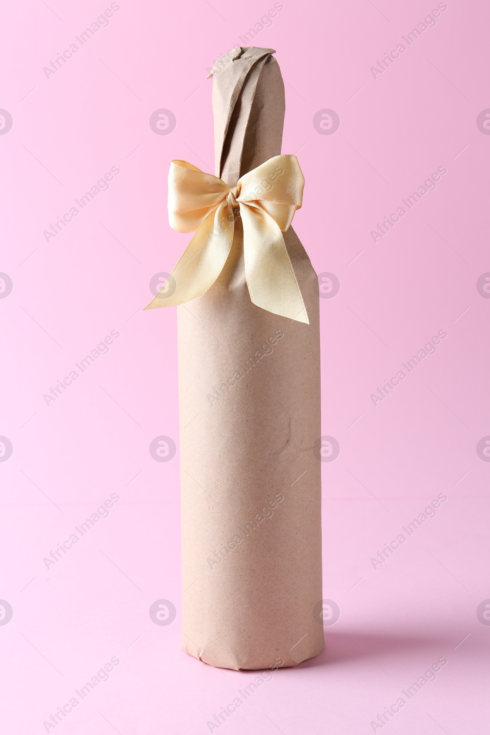 Photo of Wine bottle in burlap bag with satin bow on pink background