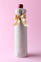 Photo of Wine bottle in burlap bag with satin bow on pink background