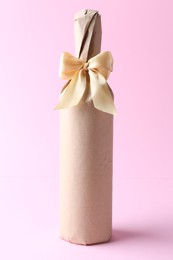 Photo of Wine bottle in burlap bag with satin bow on pink background