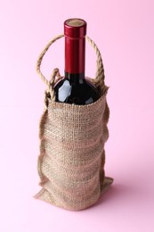 Photo of Wine bottle in burlap bag on pink background