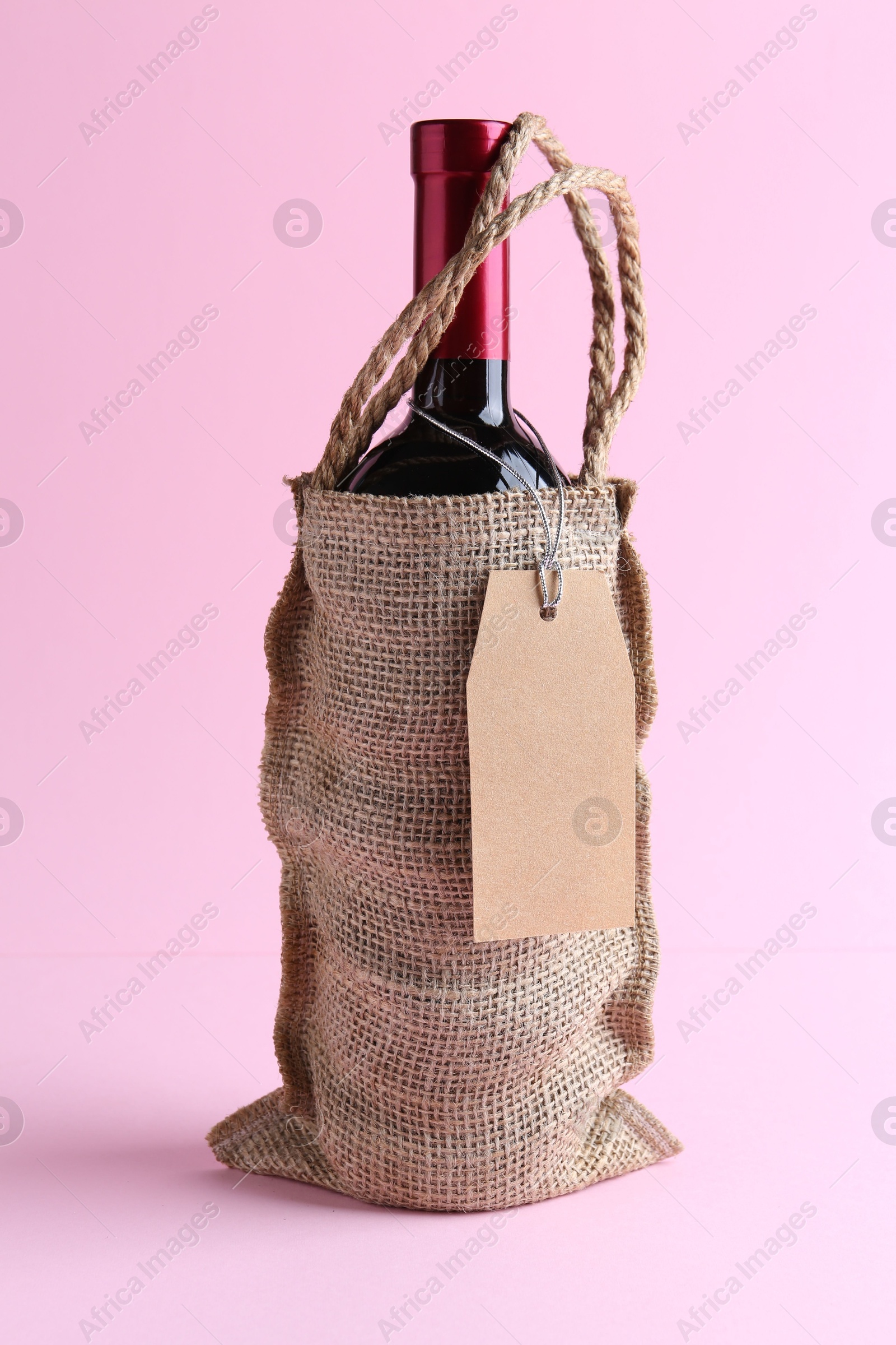 Photo of Wine bottle in burlap bag on pink background