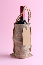 Wine bottle in burlap bag on pink background