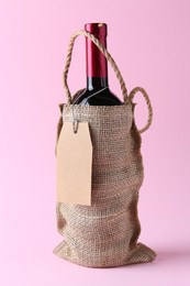 Photo of Wine bottle in burlap bag on pink background