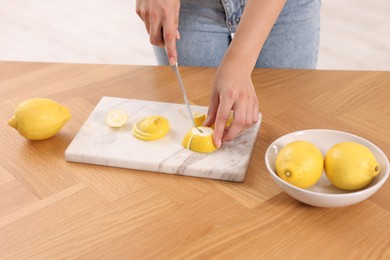 Making lemon water. Woman cutting fruit at wooden table indoors, closeup