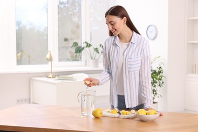 Photo of Woman squeezing lemon juice into jug with water at table indoors