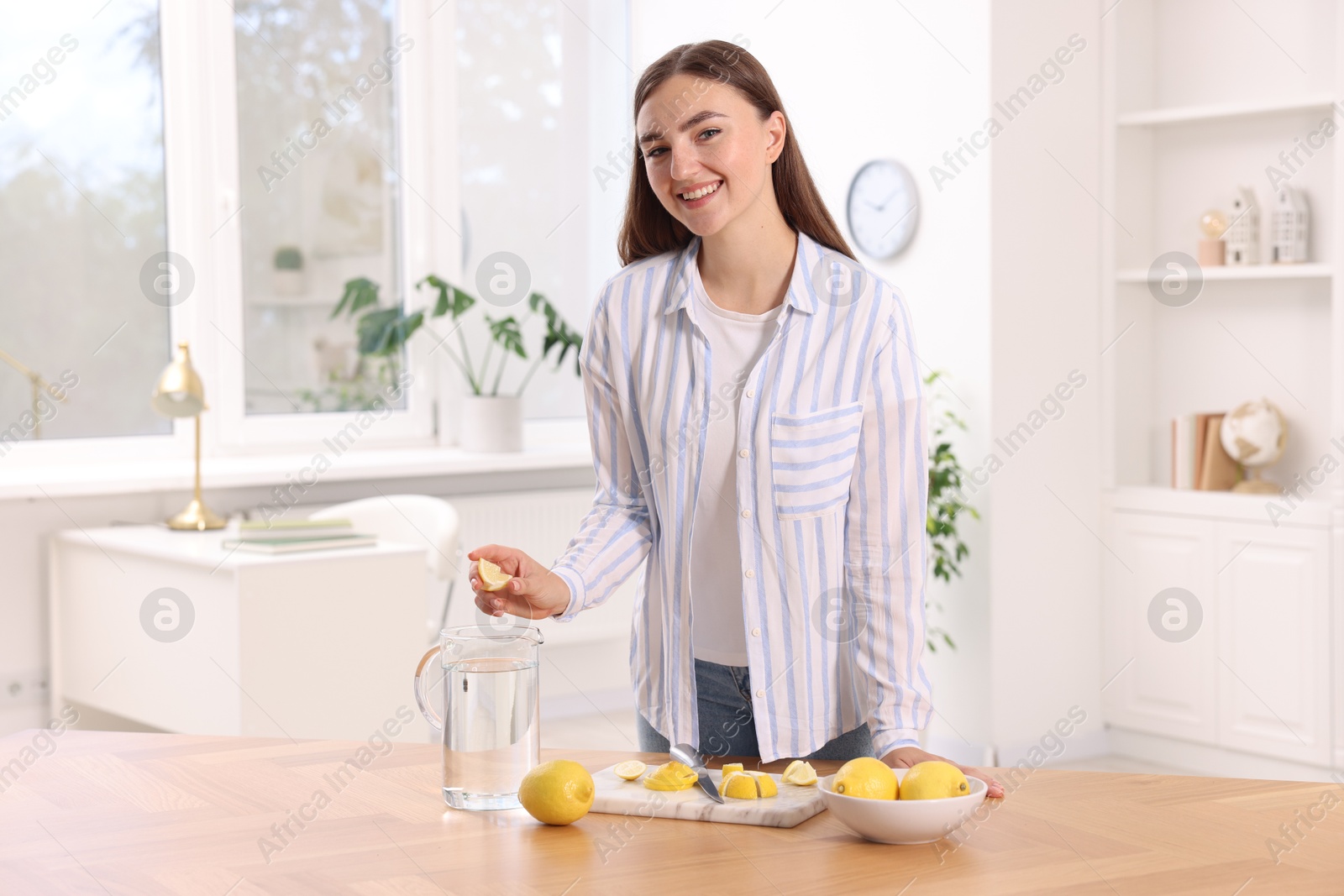 Photo of Woman squeezing lemon juice into jug with water at table indoors