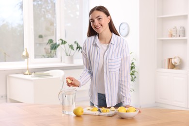 Woman squeezing lemon juice into jug with water at table indoors