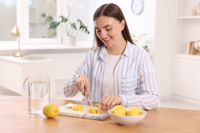 Photo of Making lemon water. Woman cutting fruit at table indoors