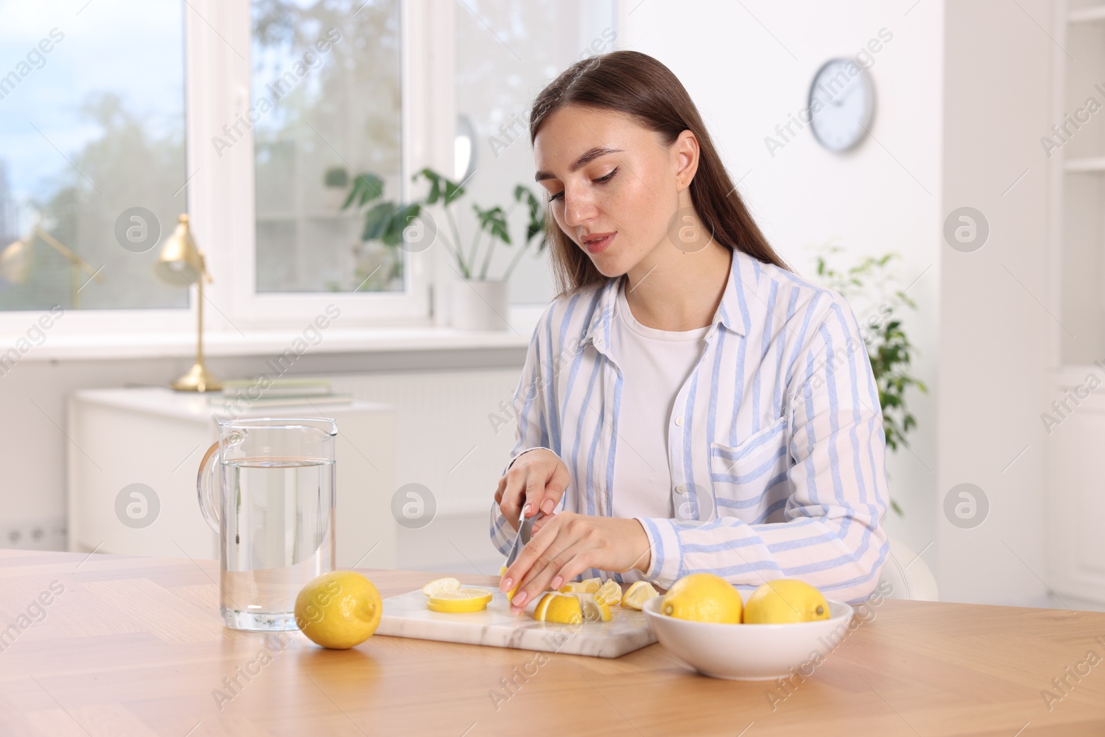 Photo of Making lemon water. Woman cutting fruit at wooden table indoors