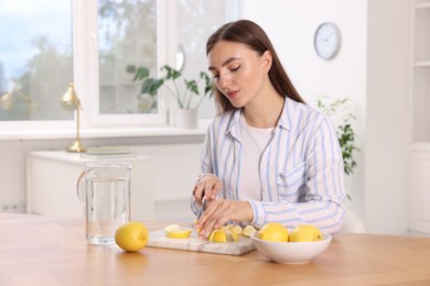 Photo of Making lemon water. Woman cutting fruit at wooden table indoors