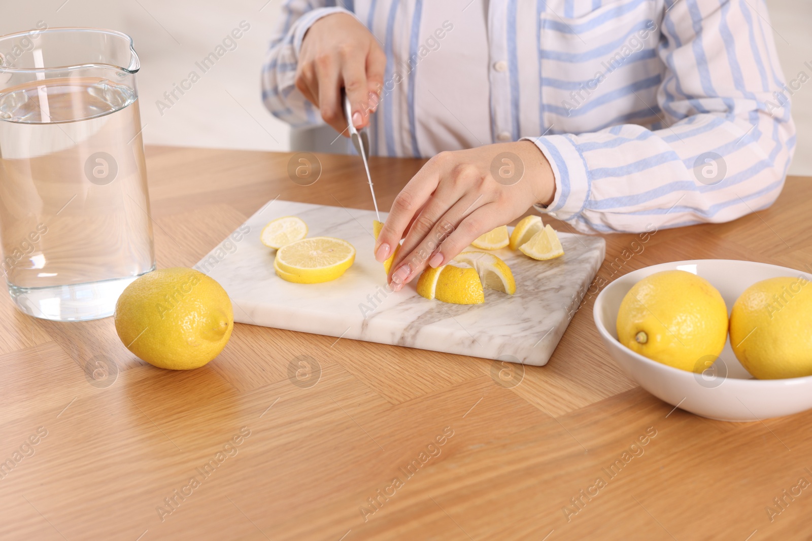 Photo of Making lemon water. Woman cutting fruit at wooden table indoors, closeup