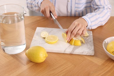 Photo of Making lemon water. Woman cutting fruit at wooden table indoors, closeup