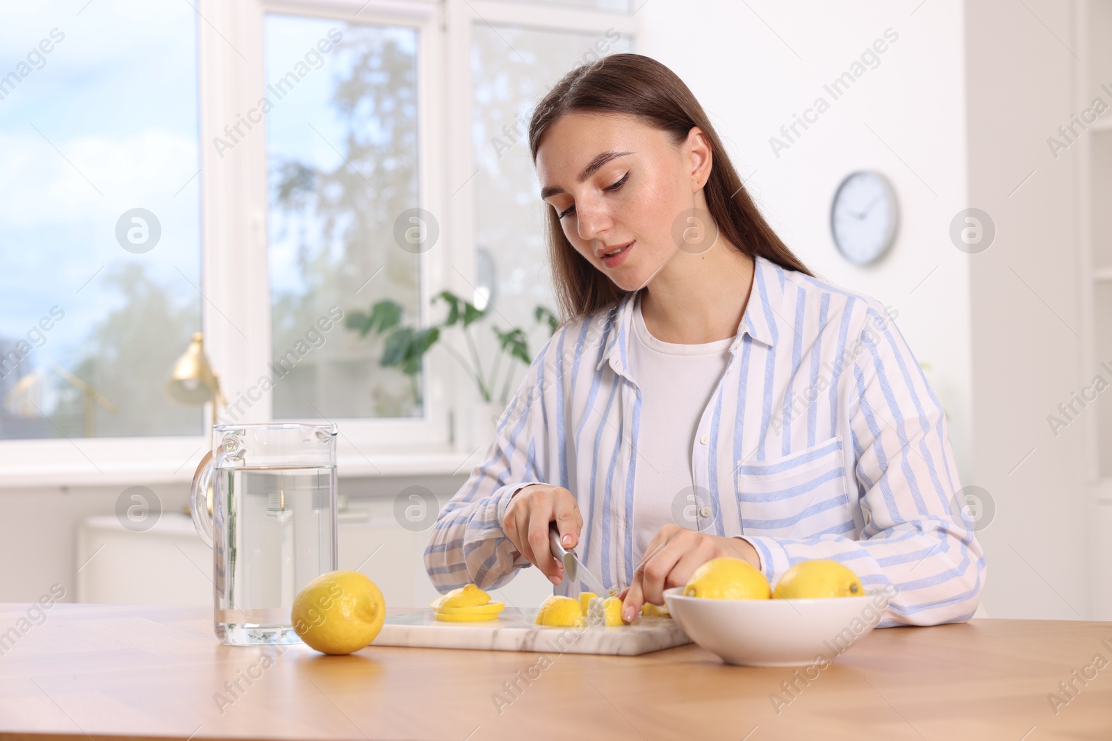 Photo of Making lemon water. Woman cutting fruit at wooden table indoors