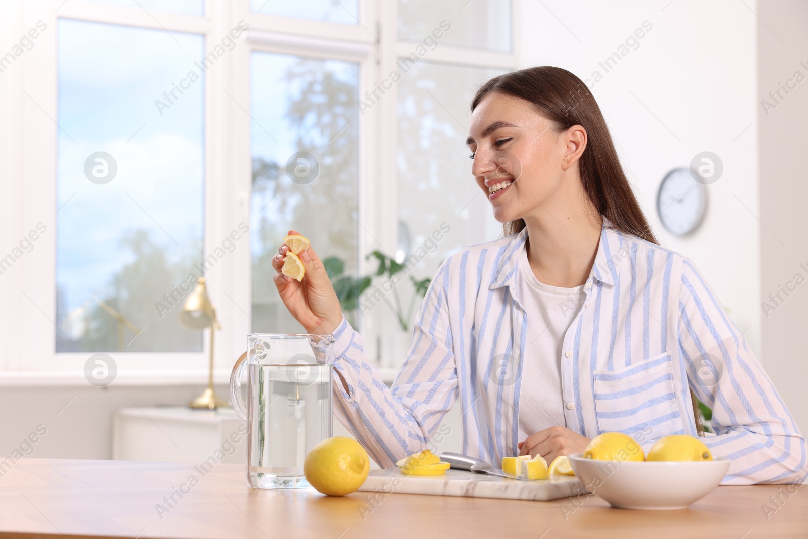 Photo of Woman squeezing lemon juice into jug with water at table indoors