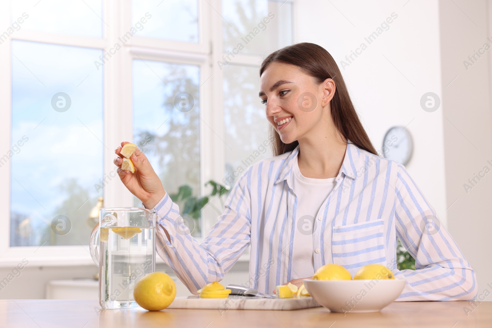 Photo of Woman squeezing lemon juice into jug with water at table indoors