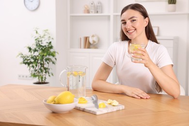 Woman with glass of lemon water indoors. Space for text