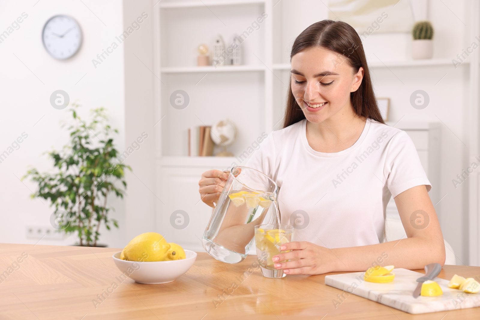 Photo of Woman pouring lemon water from jug into glass indoors. Space for text