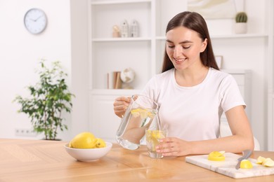 Woman pouring lemon water from jug into glass indoors. Space for text